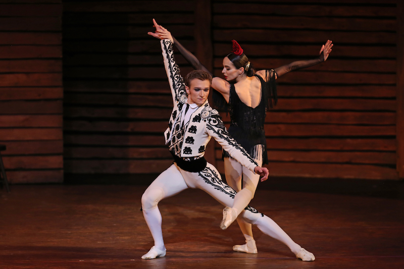 A man in a matador costume lunges while Vishneva glances back at him as she kicks her leg around his.